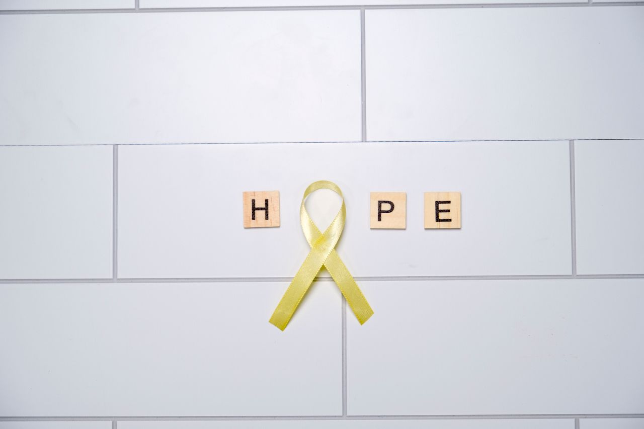 A yellow ribbon forming the word hope with tiles on a white tiled background, symbolizing awareness and support.